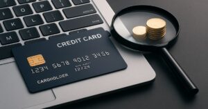 ノートパソコンの上に置かれたクレジットカードと拡大鏡のコインが並ぶ、クレジットカード比較サイト向けのアイキャッチ画像