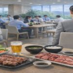 十日町市の老舗割烹弁当で食中毒発生!冬の油断が招いた事態 テーブルに焼けた焼肉とレタスが並ぶ昼食風景、グレーのスーツ姿の男性社員が座る様子