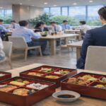 テーブルに並ぶ仕出し弁当と昼食を取る会社員の様子