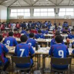 高校生ハンドボール大会で多くの選手が体育館内で弁当を食べている様子